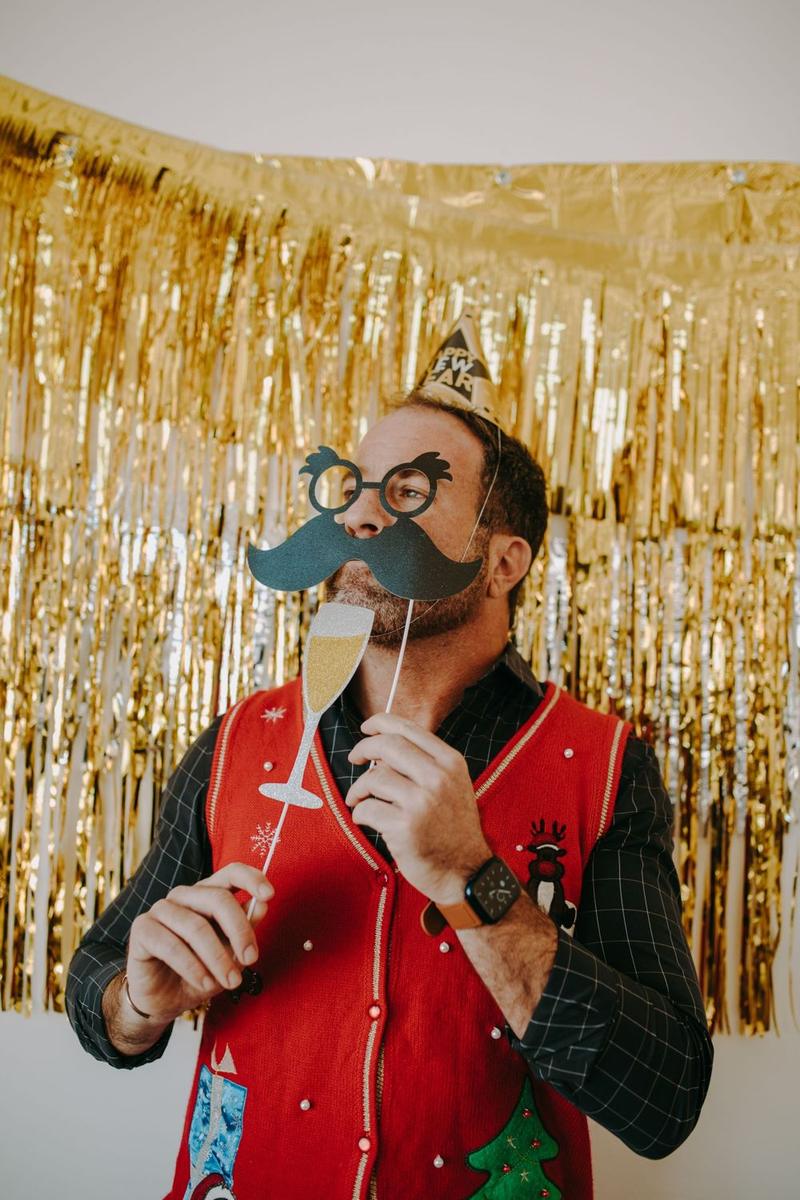 Guest with mustache and glasses props in front of a gold fringe backdrop